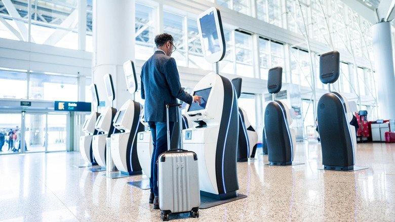 Man in suit with suitcase using automatic kiosk at airport