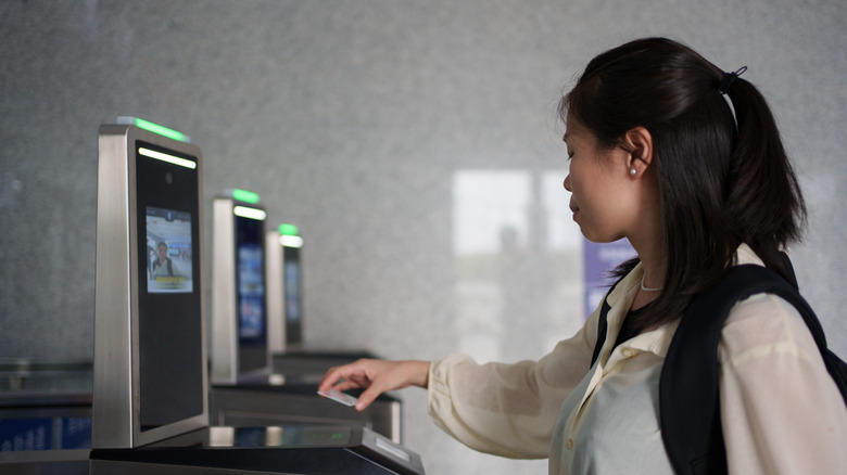 Asian woman holds ID card over facial recognition kiosk