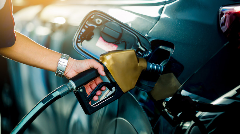 Close-up shot of an arm holding a gas pump, filling the tank of a car