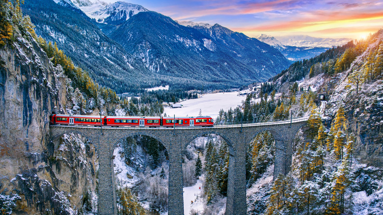 A red train crossed an historic bridge over an aqueduct in the Swiss Alps
