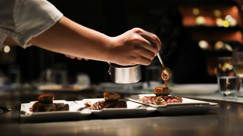 A chef spoons sauce onto waiting plates at a nice restaurant