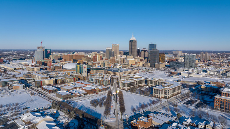 A wide aerial view of downtown Indianapolis blanketed in snow, showing the city grid, skyline, and central business district during winter