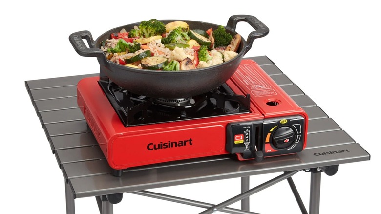 A pan filled with shrimp and vegetables sauteing on a red camping stove.