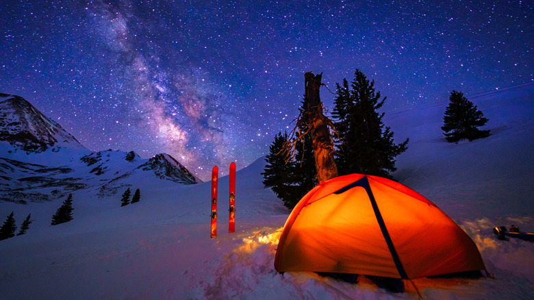 A tent is pitched in the snow high on a mountain ridge with stars above