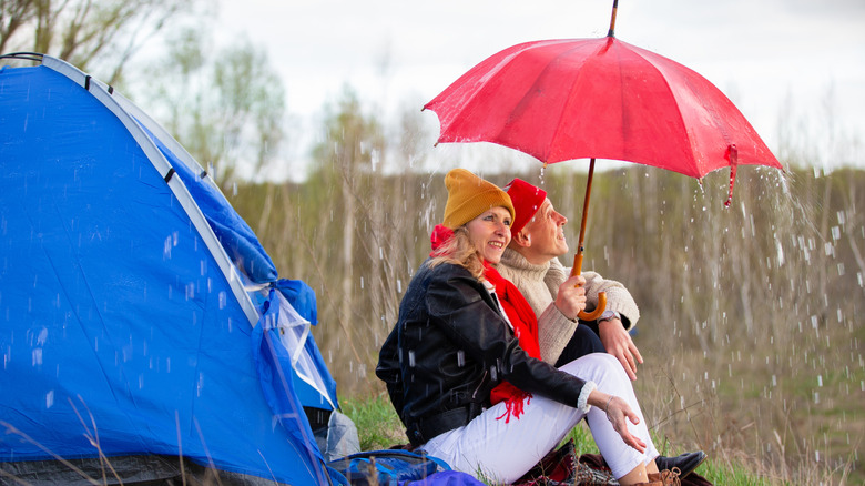 An elderly couple under an umbrella outside a tent in the rain