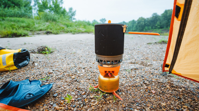 A portable camping stove on the ground near a tent