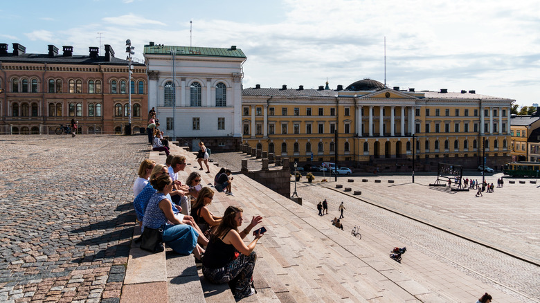 A group of people sitting on the steps in a Helsinki square in Finland