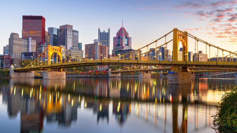 The Three Sisters Bridges span a river in front of Downtown Pittsburgh at dusk