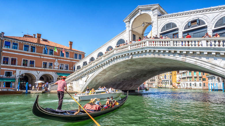 Gondola with people going under Rialto Bridge Venice sunny day