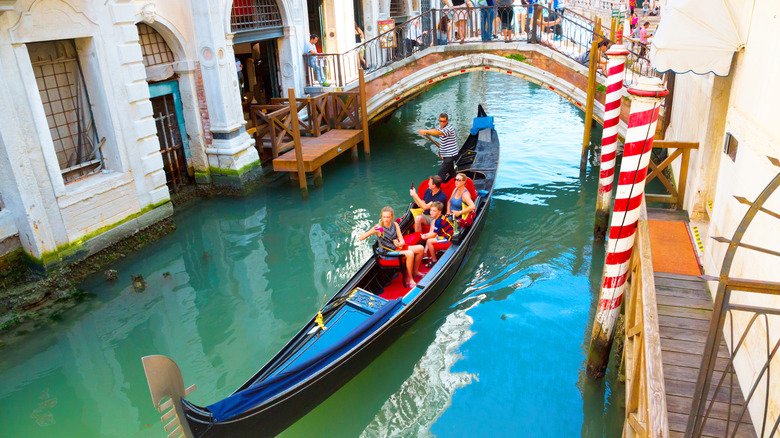 Group of people on a gondola pass under bridge in narrow canal in Venice