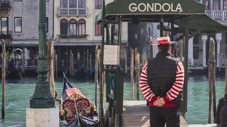 Gondolier stands at gondola station with back to camera facing the canals