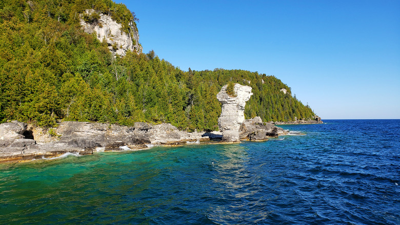 Turquoise water with large rock formation on the shore at Tobermory, Candada
