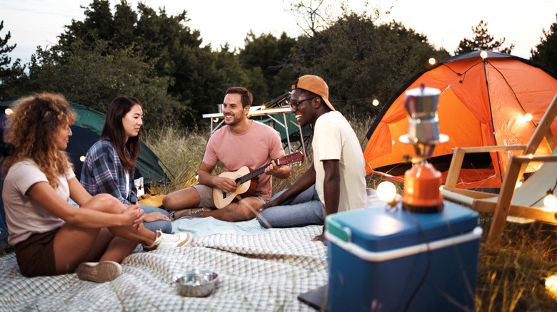 Group of friends camping with stove, tents, cooler, guitar