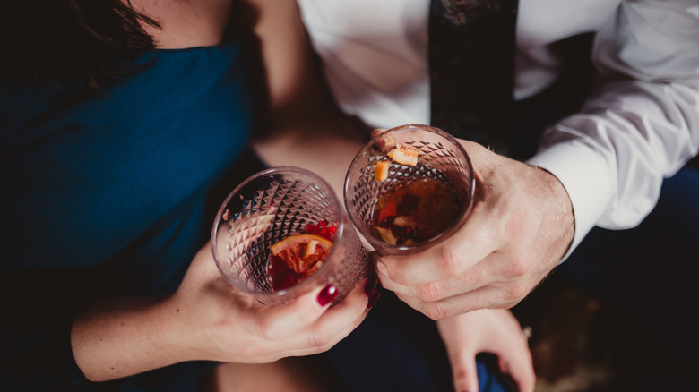 A man and woman cheers with negronis at a sultry lounge.