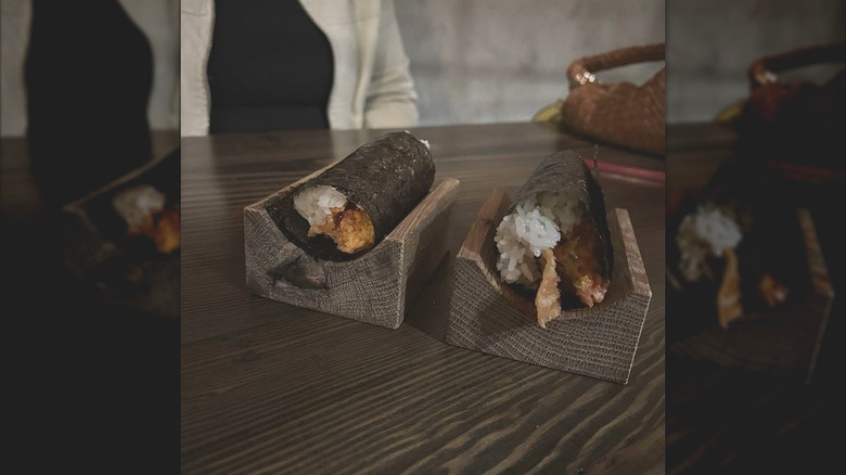 Two hand-rolled sushi rolls in wooden holders with a diner seated at a table at Lou's Sushi in Midtown Sacramento.