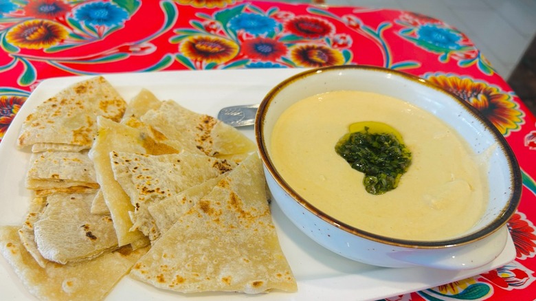A floral tablecloth set with a bowl of hummus and flatbread cut into triangles at Meza California.