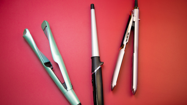 Overhead view of curling irons and hair straighteners on a red background