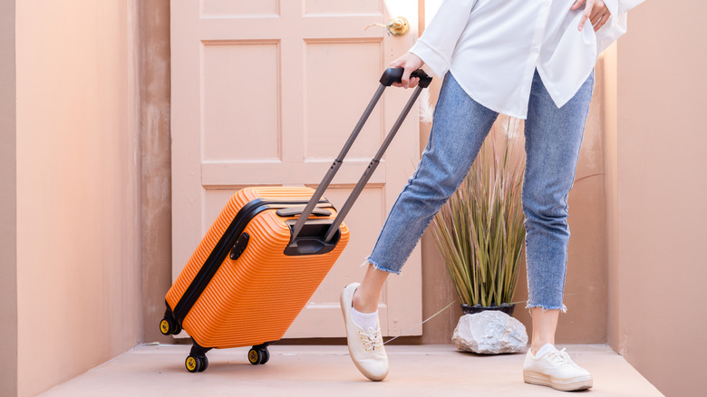 Woman rolling her orange luggage out of the house
