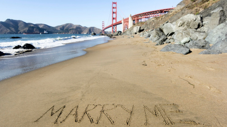 "Marry me" written in the sand on a beach with the Golden Gate Bridge in the background