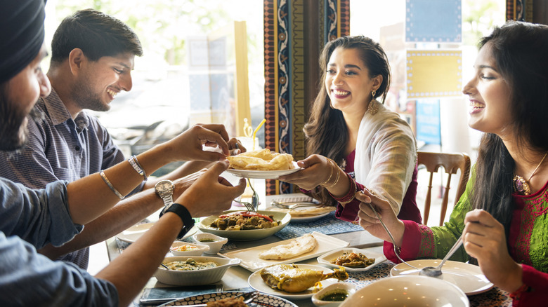 A group of four Indian friends, smiling and laughing and enjoying a variety of dishes at an unidentified Indian restaurant