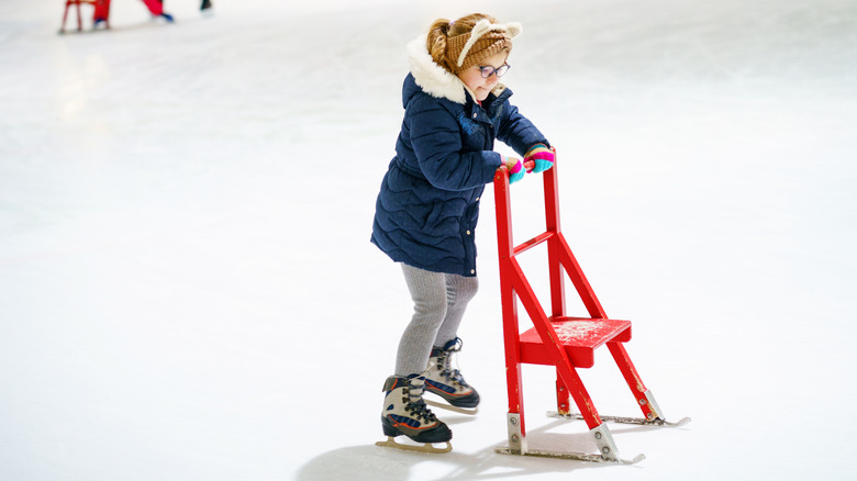 A little girl learning to ice skate with a device to stay upright.