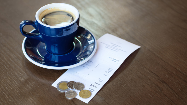A small blue cup of coffee with Euro coins and a receipt on table