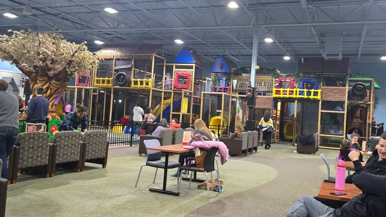 A large, colorful indoor children's play gym with parents supervising from chairs.