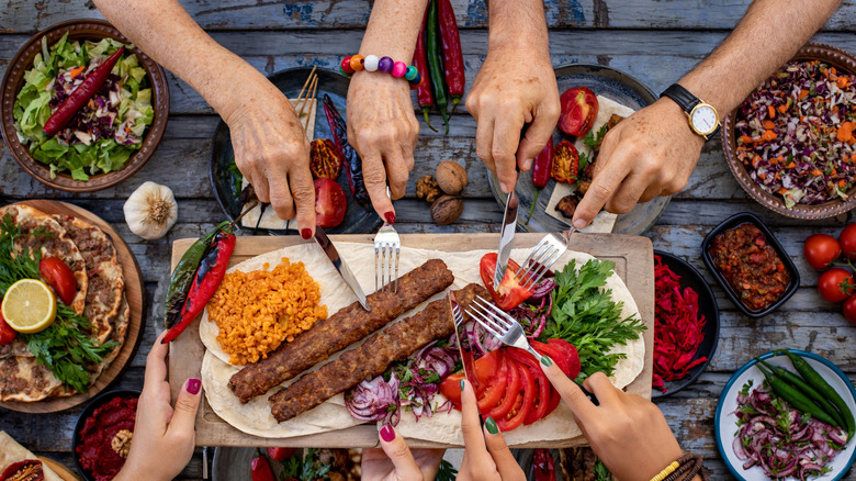 A photo showing four sets of hands reaching in and sharing a mezze platter of various Lebanese dishes