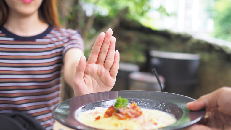 A person raising her hand up to refuse food being offered to her
