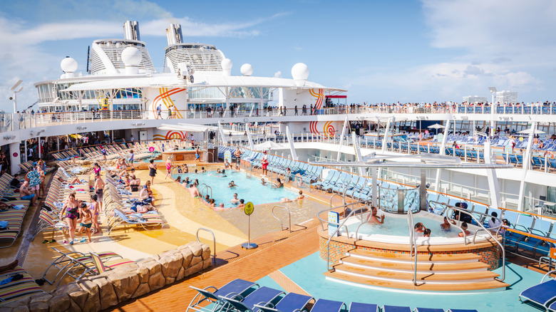 People on the pool and sun deck on a large cruise ship under a clear blue sky