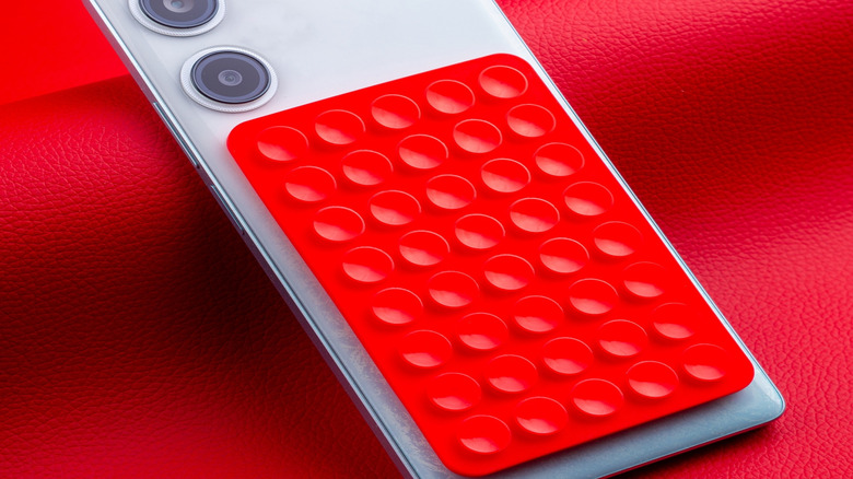 Close-up of a modern white smartphone, with a silicone adhesive pad stuck to its case, for easy mounting on a wall or other flat surface