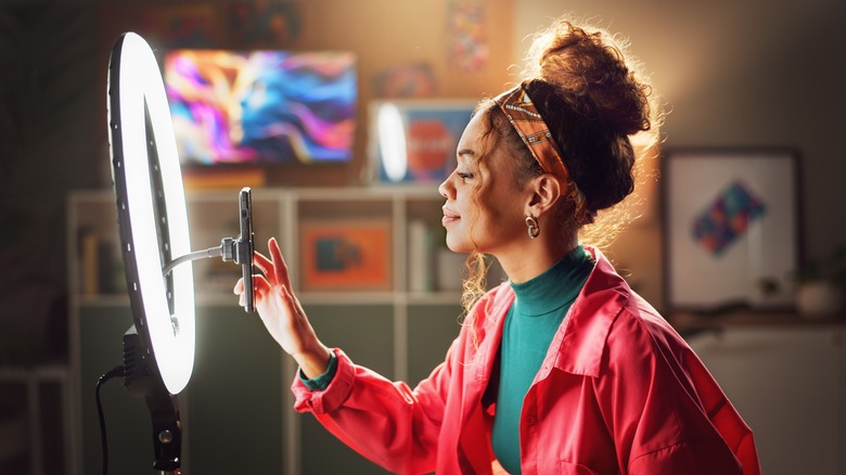 A young female influencer sets up her mobile phone with a ring light for video recording and content creation at home