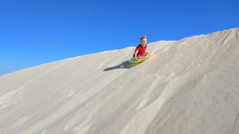 A young child in a red shirt sledding down a sand dune at Monahans Sandhills State Park