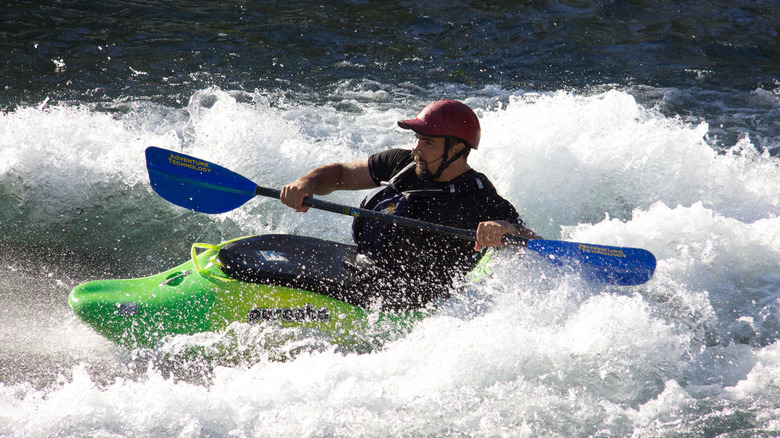 A man in a green raft holding up a double-sided paddle on the San Marcos River.