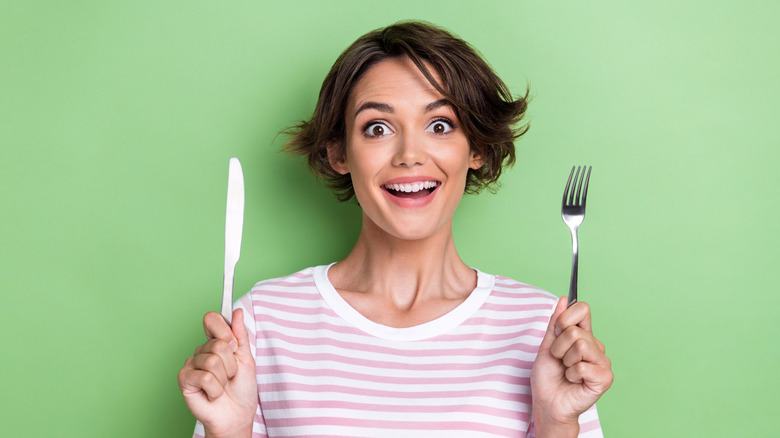 A woman holds a knife and fork in her hands