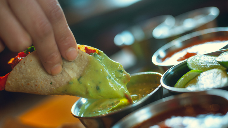 A woman dips a taco in green salsa