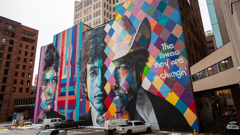 A vibrant Bob Dylan mural in Minneapolis with three Dylan faces, rainbow colors, a guitar, and song lyrics