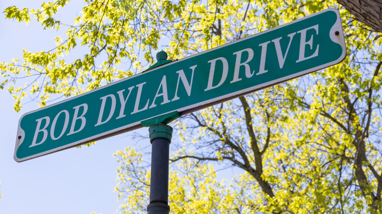 A street sign saying Bob Dylan Drive with leaves on branches behind it