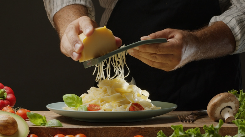 A chef grates cheese onto a plate of pasta