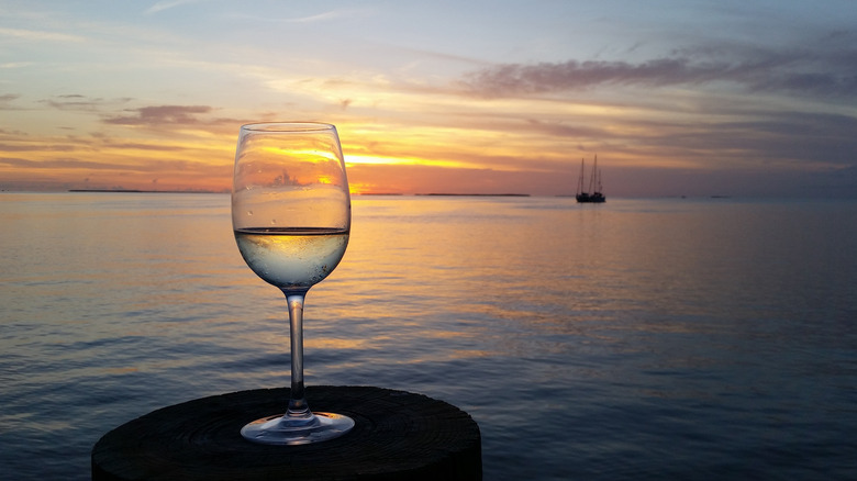 Glass of wine on a restaurant table in Florida, looking out toward the bay at sunset with a silhouette sailboat in the distance