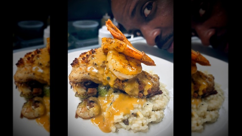 Chef peeking behind seafood plate with shrimp, fish, and risotto