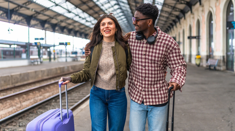Couple pushing suitcases along a train station platform