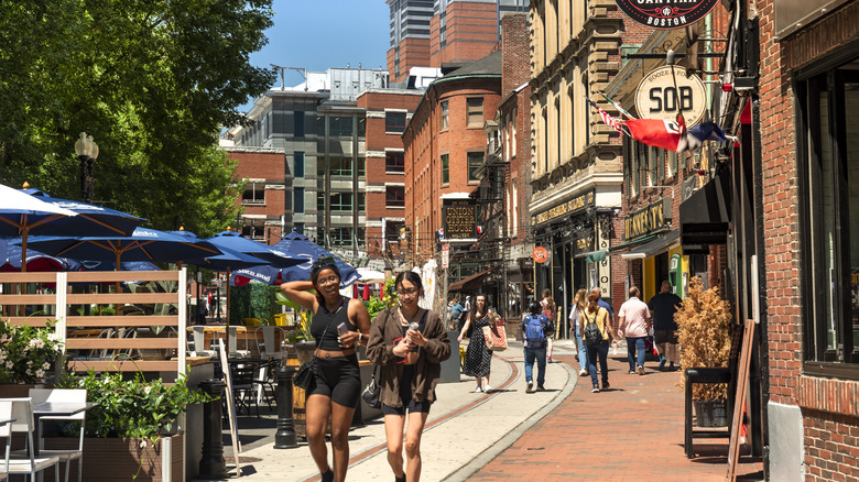 Tourists walkin down a city pavement lied with brick buildings with restaurant signs