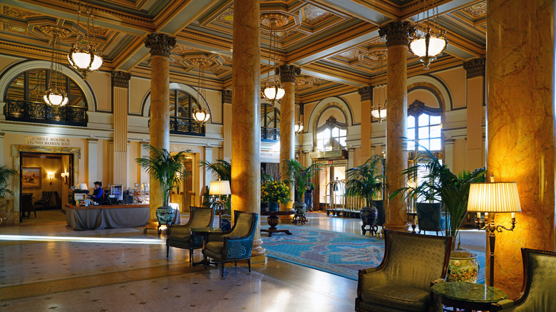 Lobby of The Willard InterContinental, with marble floors and columns, white-accented yellow walls, green armchairs, and potted plants under hanging lights