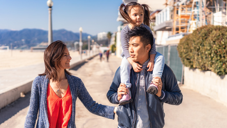 Parents walking together on vacation; Dad is holding their daughter on his shoulders