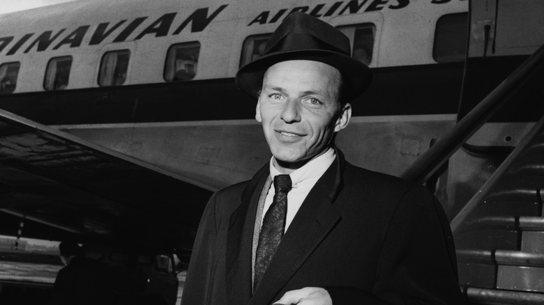 Black and white photograph of Frank Sinatra standing in front of an airplane at a London airport