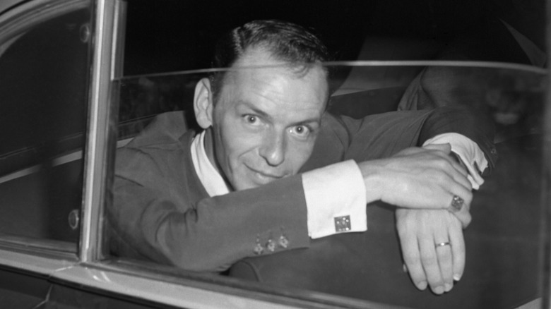 Black and white photo of Frank Sinatra leaning out of a car window with his hands crossed