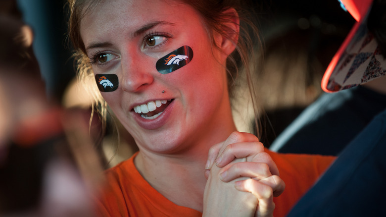 A Denver Broncos fan with team stickers on her face, holding her hands in hope during a game.