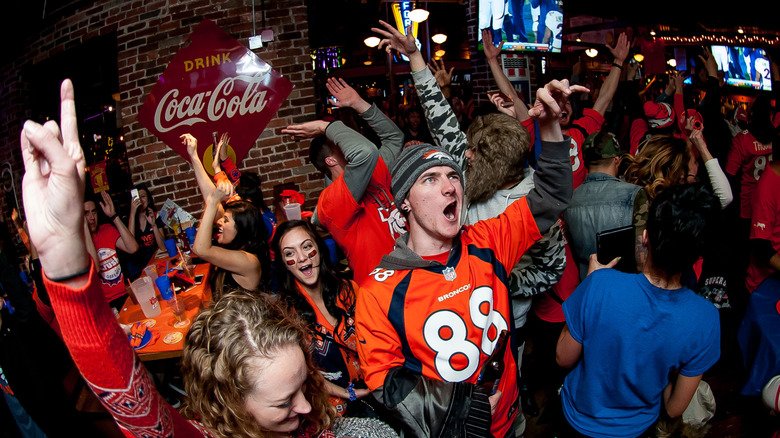 Denver Broncos fans wearing team jerseys and merch celebrating during a Broncos game in a Denver bar.