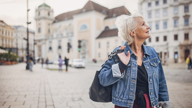 Older woman alone on the streets of Vienna looking up at the tall, sand-stone buildings surrounding her